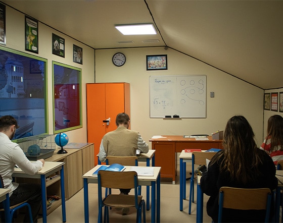 http://La%20photo%20montre%20une%20salle%20de%20classe.%204%20élèves%20sont%20assis%20à%20une%20table%20devant%20le%20bureau%20du%20professeur.