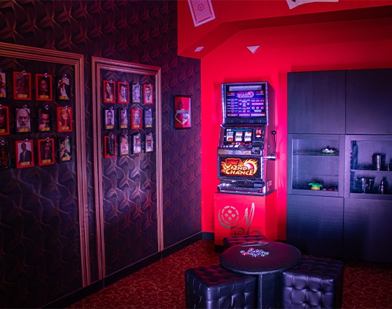 http://C'est%20une%20photo%20d'un%20casino.%20Au%20milieu%20de%20la%20pièce%20se%20trouve%20une%20petite%20table%20avec%20des%20jetons%20de%20poker.%20Dans%20le%20fond%20se%20trouve%20une%20armoire%20ainsi%20qu'une%20machine%20à%20sous.%20Des%20portraits%20sont%20affichés%20sur%20le%20mur%20à%20gauche.
